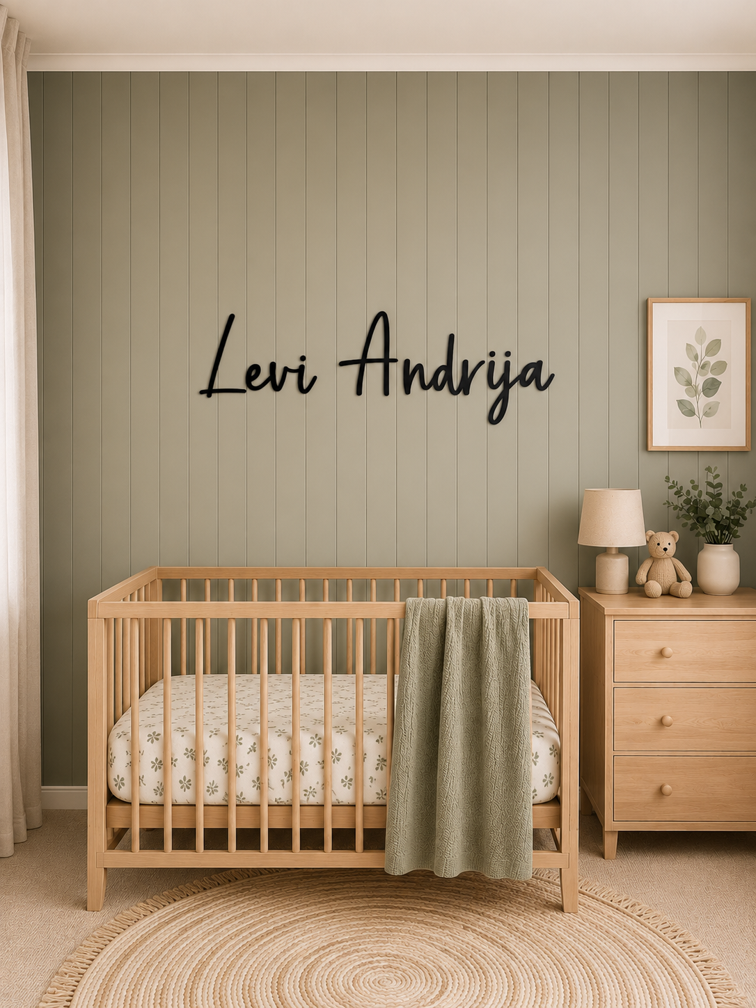 Personalised black acrylic nursery name sign mounted above a timber cot on a sage green feature wall