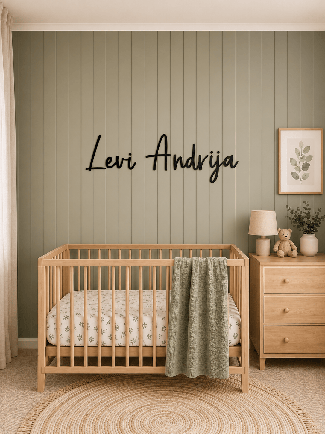 Personalised black acrylic nursery name sign mounted above a timber cot on a sage green feature wall
