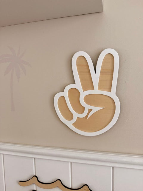 Wooden Peace Sign with white Acrylic outside hanging against a beige wall