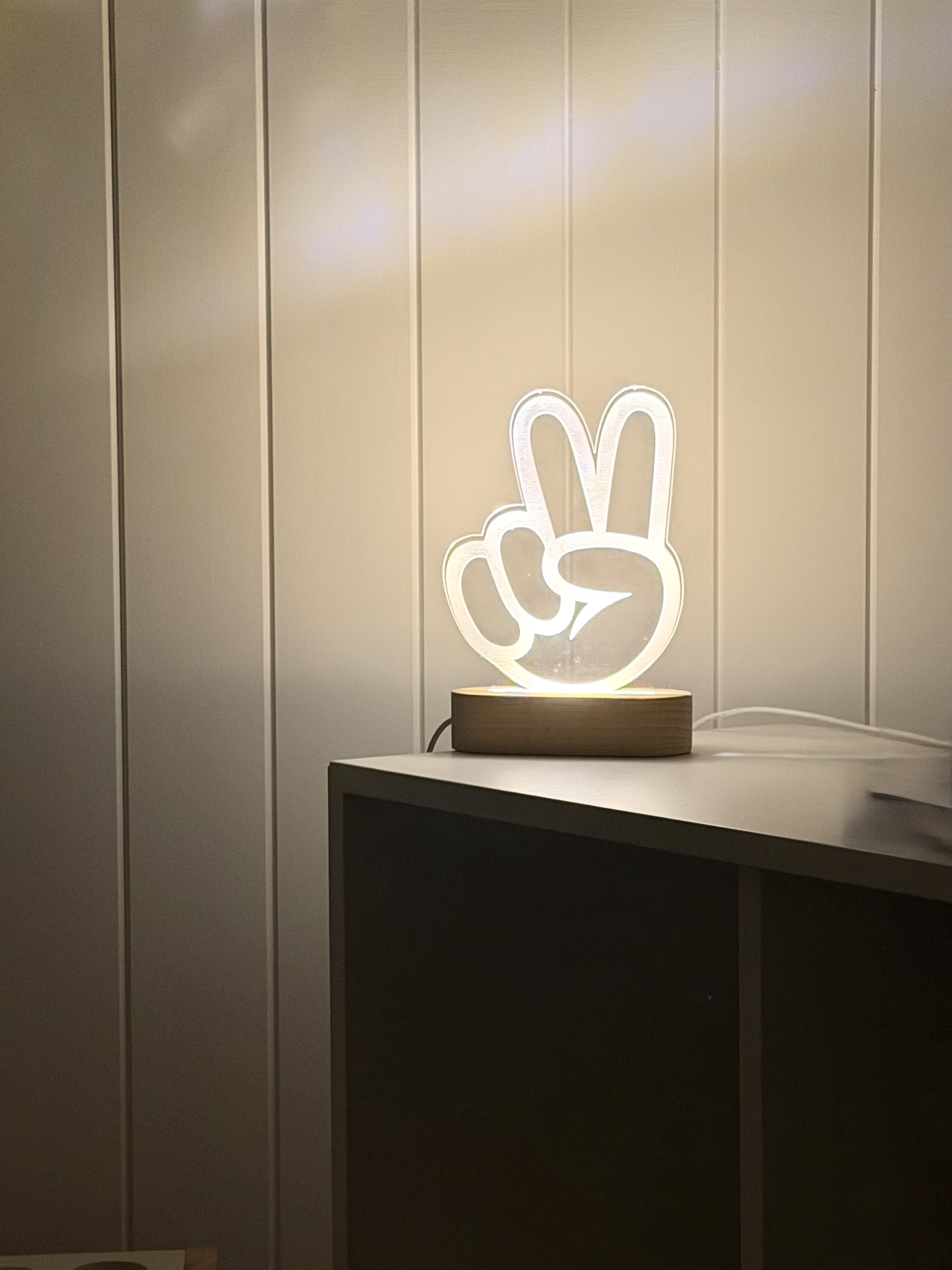 Peace hand engaved on light with timber stand against panelled wall