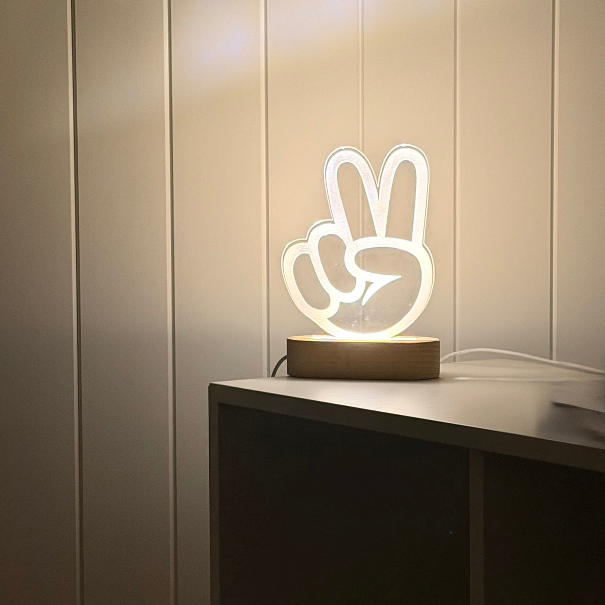 Peace hand engaved on light with timber stand against panelled wall