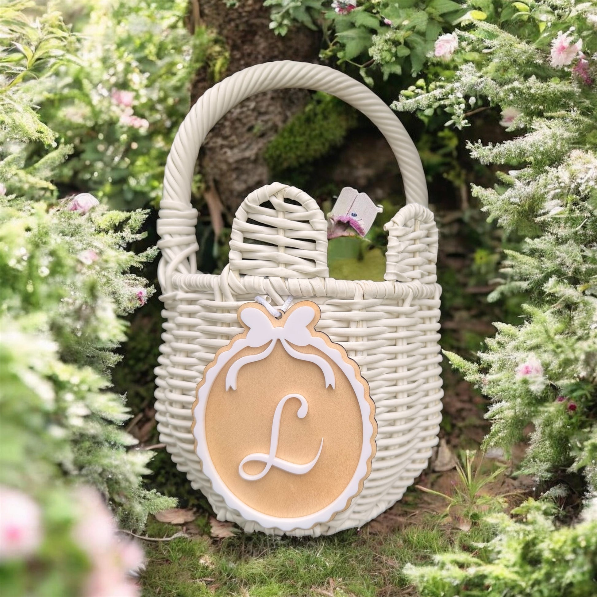 Personalised Easter Basket Tag with custom initial L and bow detail attached to white wicker basket in garden setting