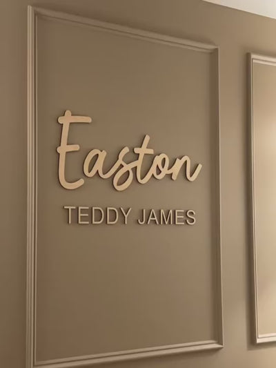 Close up of Easton Teddy Jame Timber name sign on wall with a gold cot in front of it.